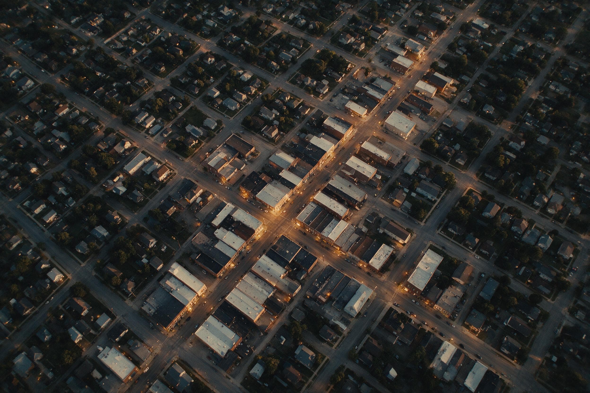 Aerial view of a small town at dusk, its street grid and lit main street seen from directly overhead